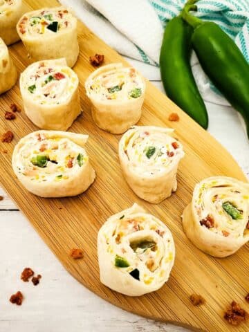 Cream cheese pinwheels sliced on cutting board with bacon pieces.