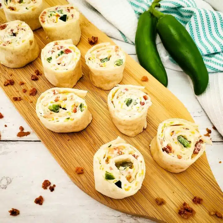 Cream cheese pinwheels sliced on cutting board with bacon pieces.