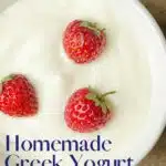 Greek yogurt in a white bowl with whole strawberries and stems.