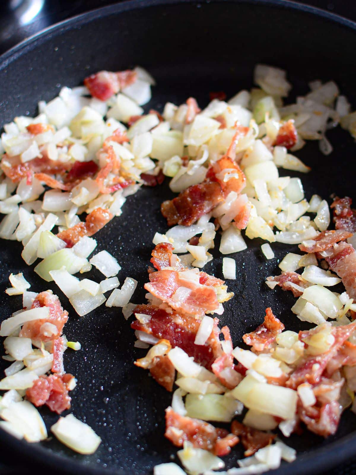 frying bacon with onion in pan.