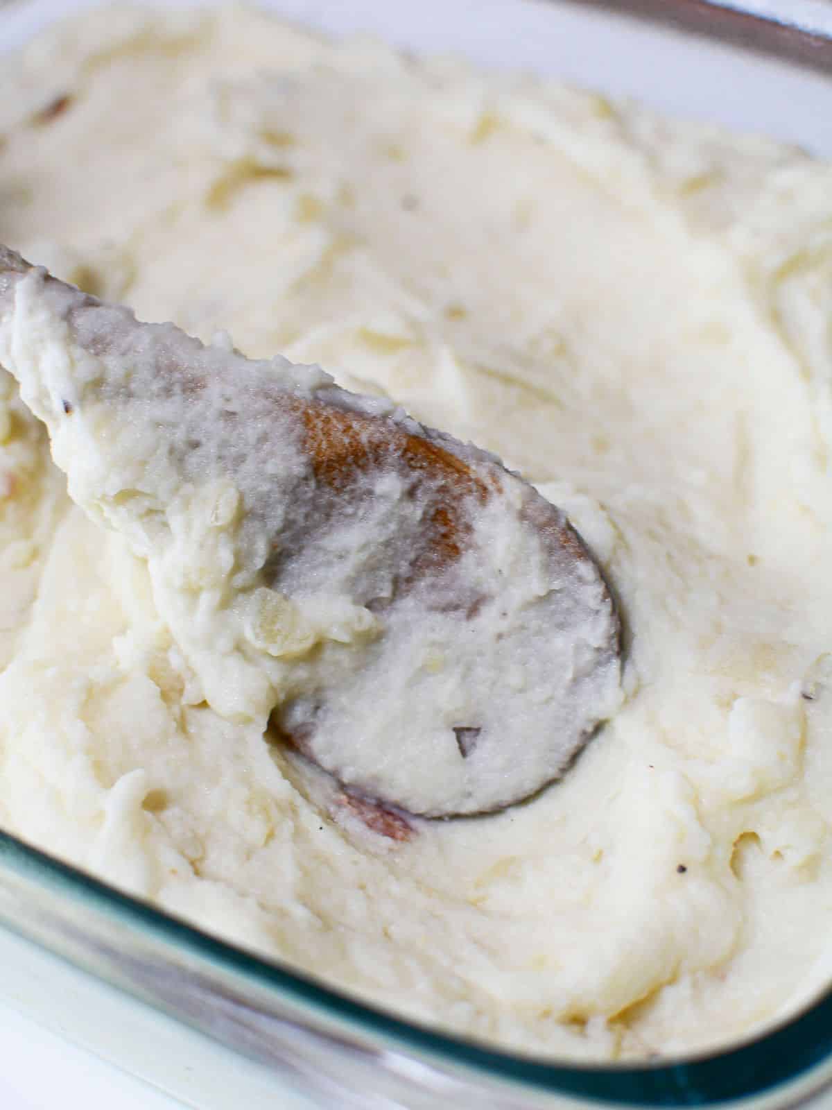 Mashed potatoes in casserole dish with wooden spoon.