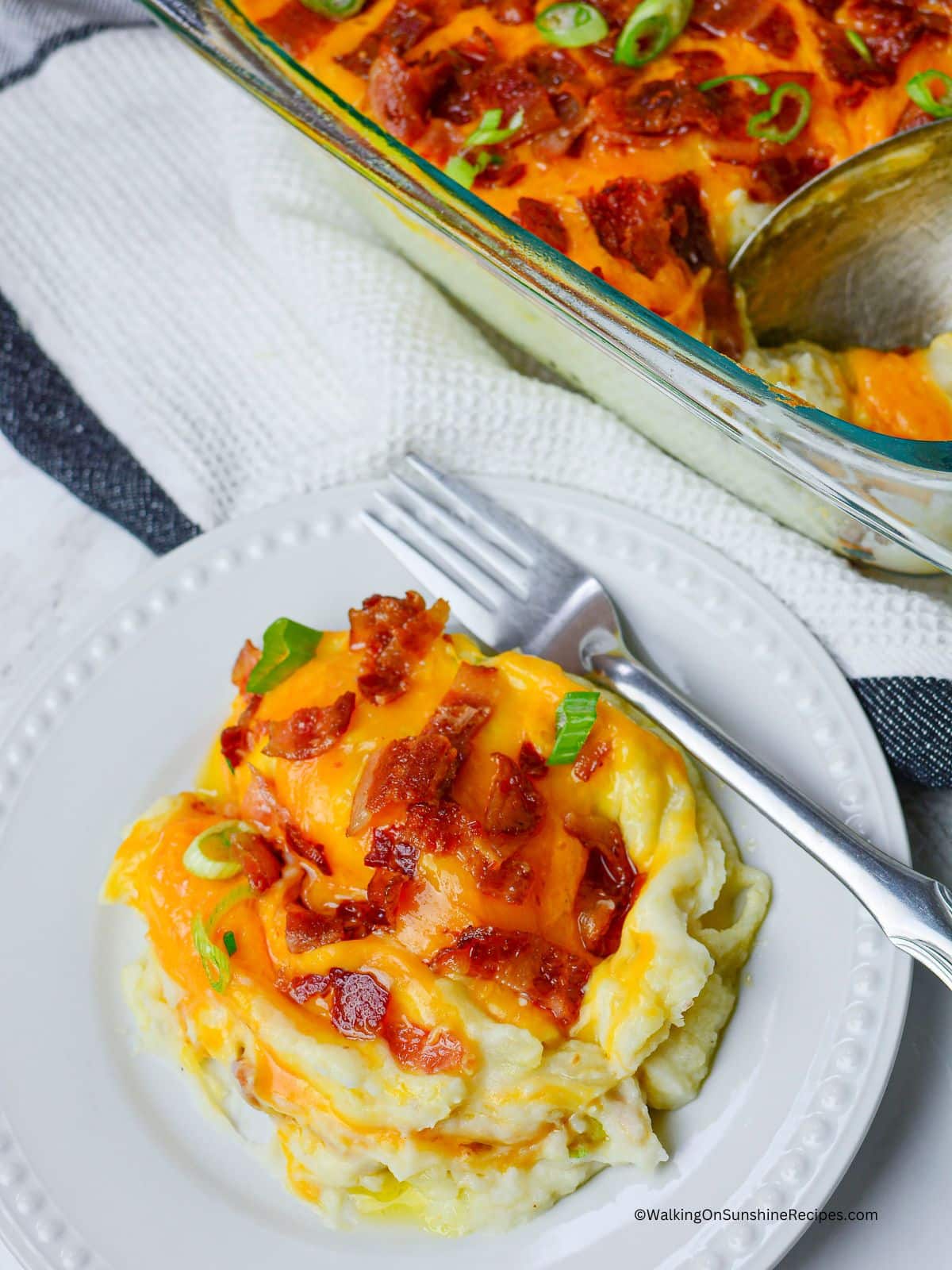 Mashed potato casserole with cheese, bacon and onions on white plate.