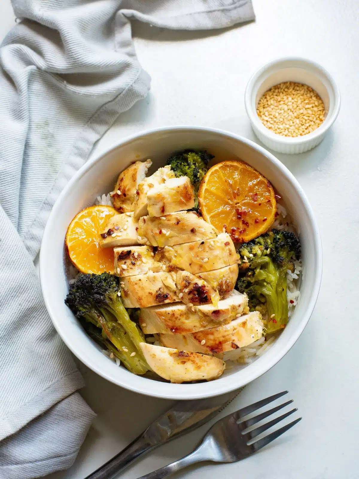 Sliced chicken cutlet, broccoli, and orange sliced served over rice in a white bowl.