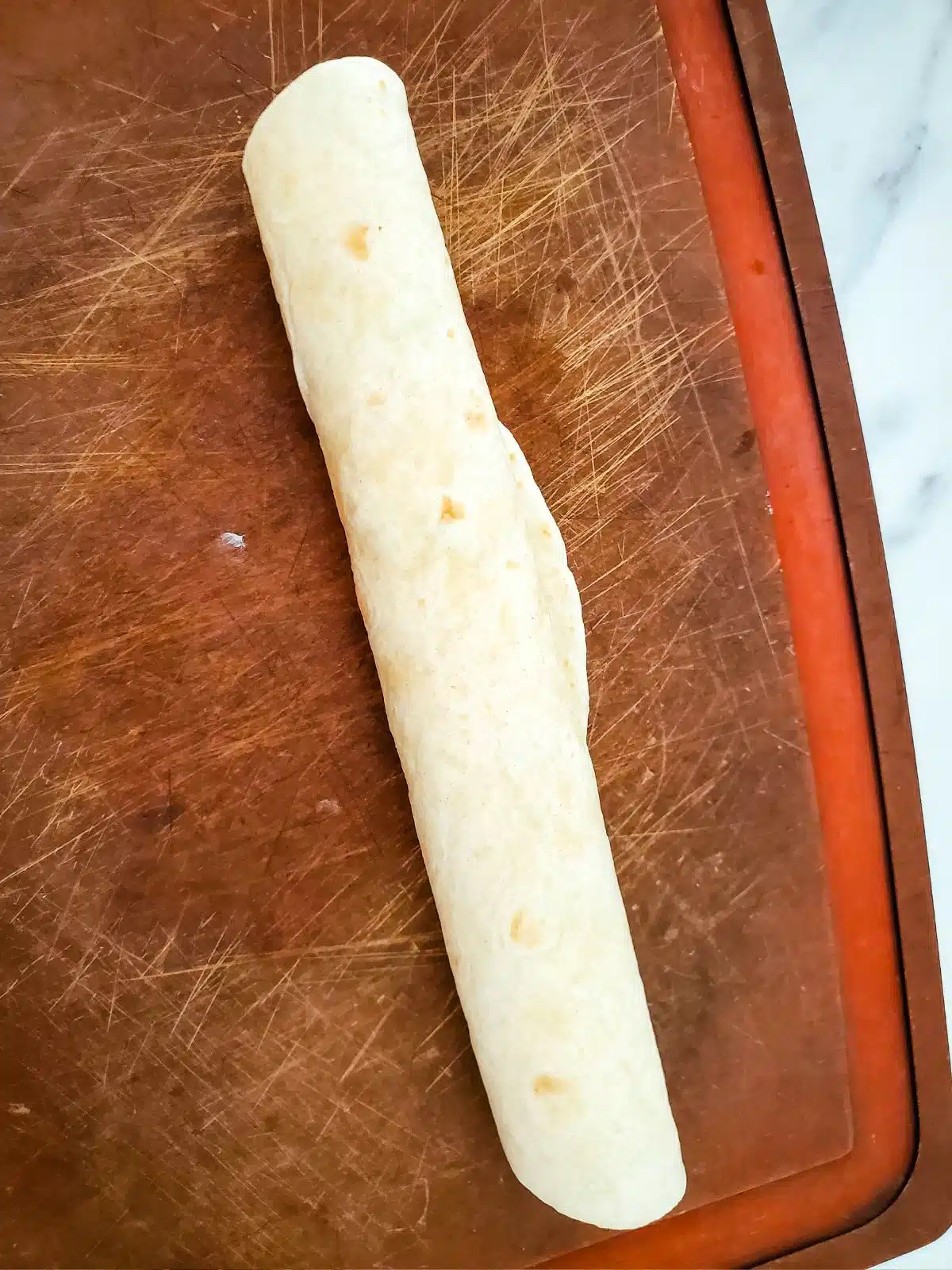flour tortilla rolled up on cutting board.