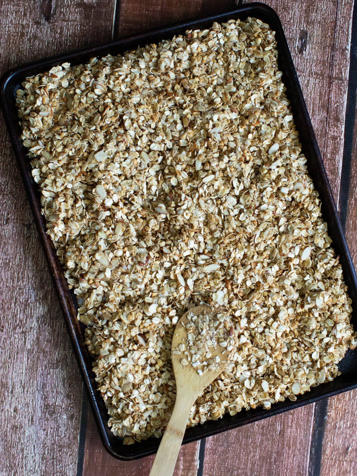 unbaked granola on baking tray with wooden spoon.