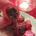 Strawberries filled with chocolate being held over plate.