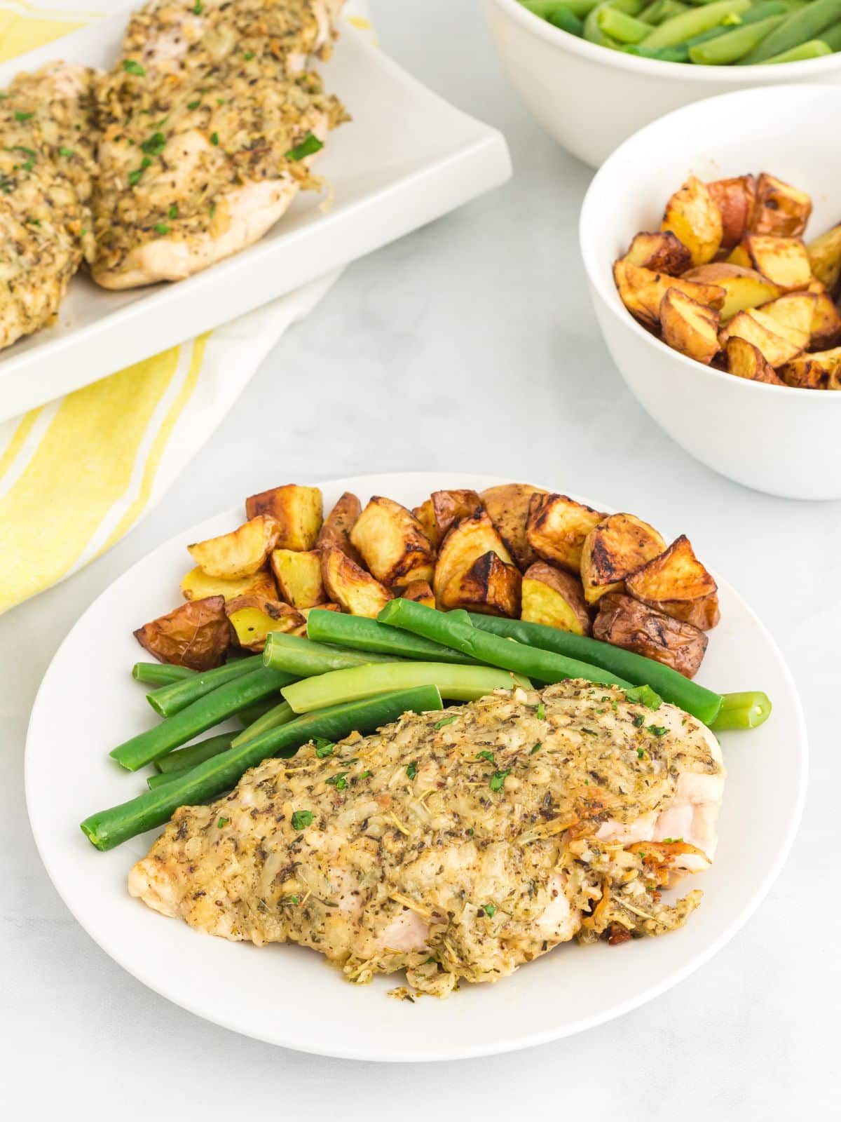 Garlic chicken on white plate with green beans and roasted potatoes.