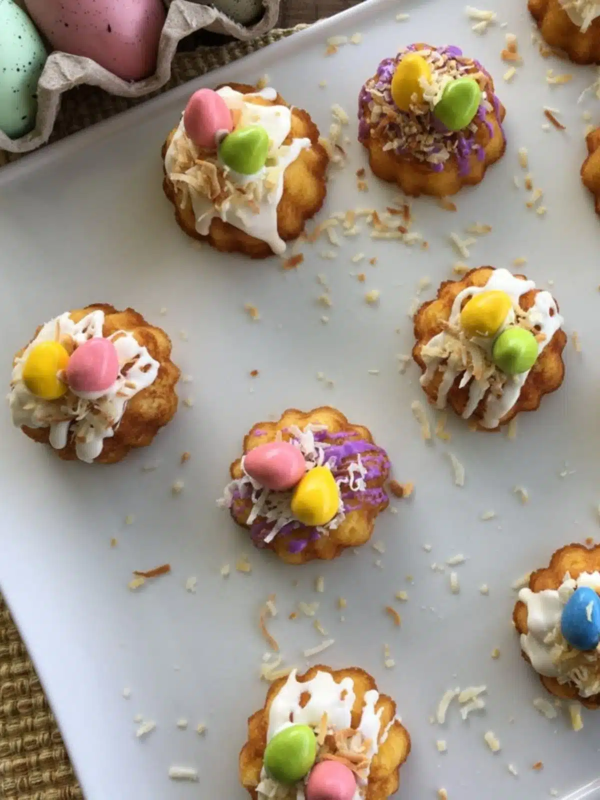 Vanilla mini bundt cakes with coconut, icing and candies on white plate.
