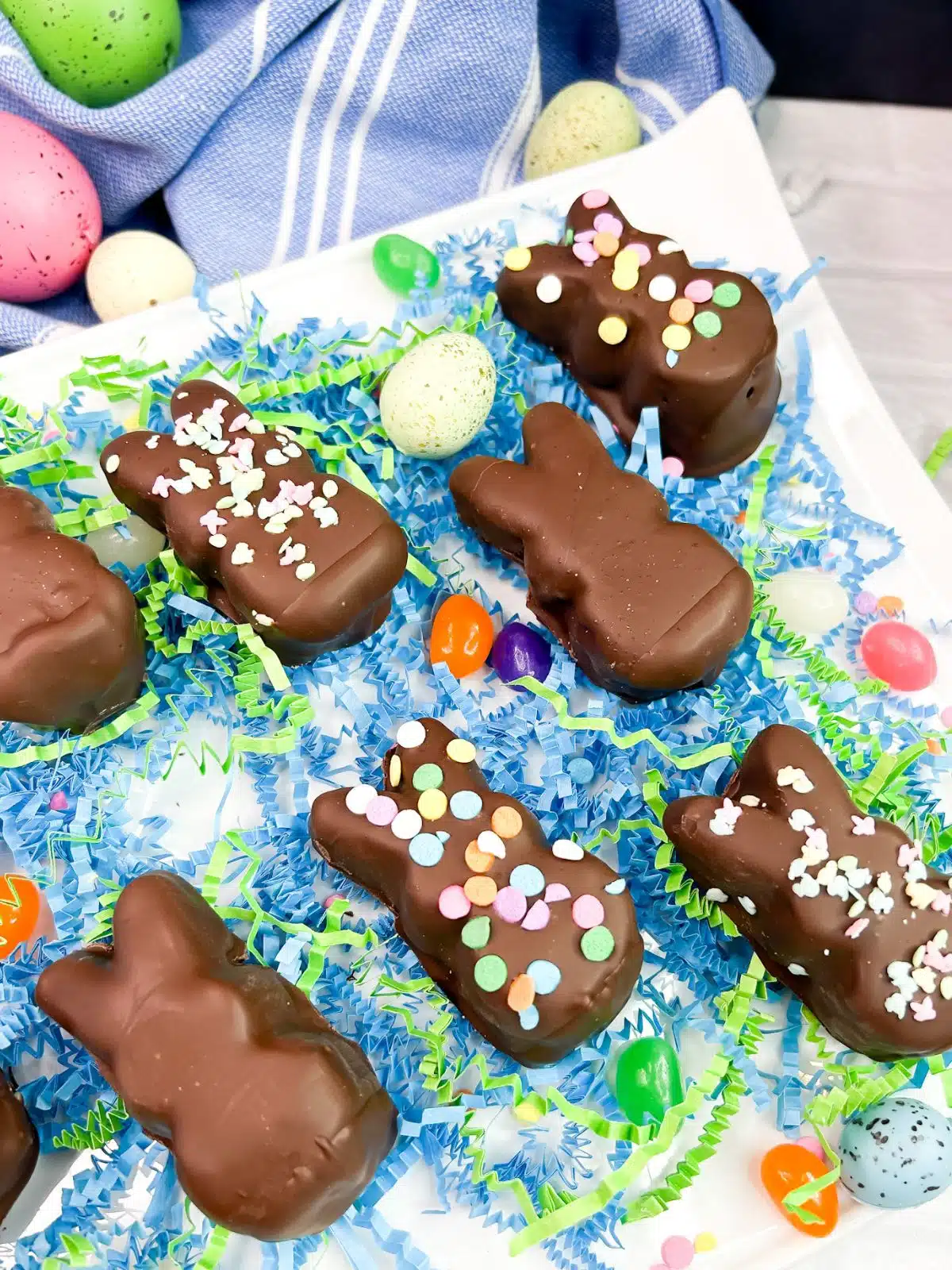 chocolate dipped marshmallow bunny Peeps on plate with jelly beans and plastic eggs.