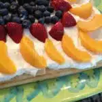 fruit tart made with crescent rolls, peaches, strawberries and blueberries on green platter.