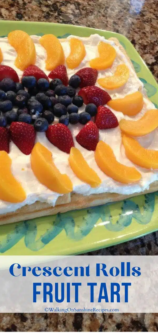 fruit tart made with crescent rolls, peaches, strawberries and blueberries on green platter.