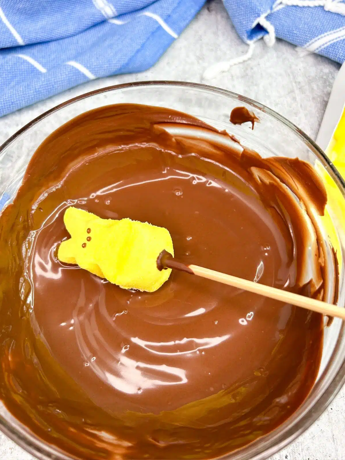 bowl of melted chocolate and yellow marshmallow Peep on bamboo stick.