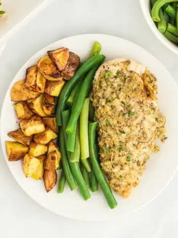 Garlic butter chicken with roasted potatoes and green beans on white plate.