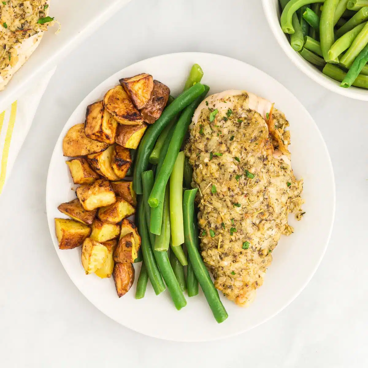 Garlic butter chicken with roasted potatoes and green beans on white plate.