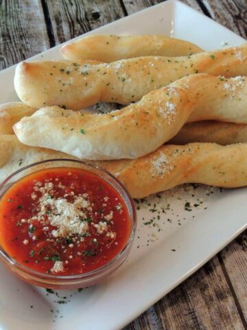 semi-homemade breadsticks baked on serving tray with small bowl of marinara sauce.