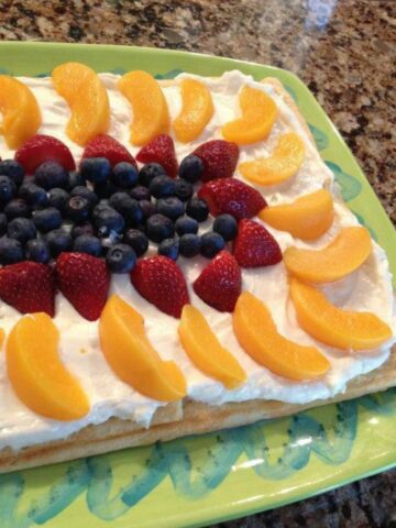 fruit tart with peaches, strawberries, blueberries and cream cheese frosting.