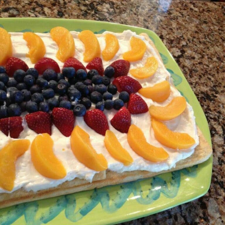 fruit tart with peaches, strawberries, blueberries and cream cheese frosting.