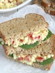 egg salad sandwich on wheat bread with spinach leaves and bacon.