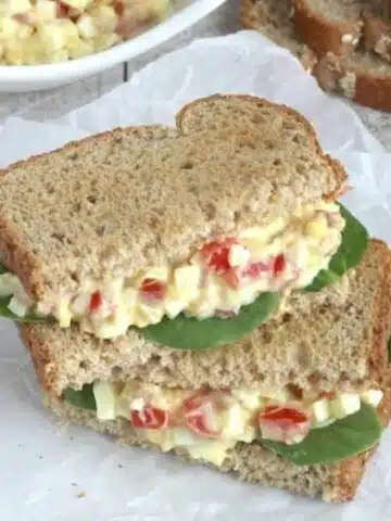 egg salad sandwich on wheat bread with spinach leaves and bacon.
