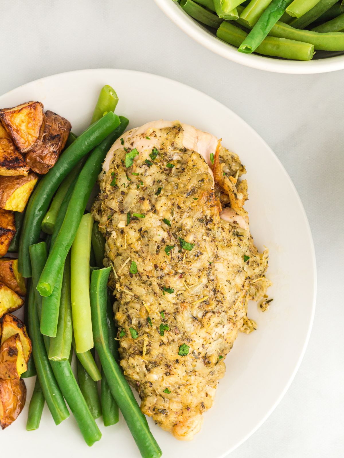 baked chicken on plate with herbs. Green beans on side.