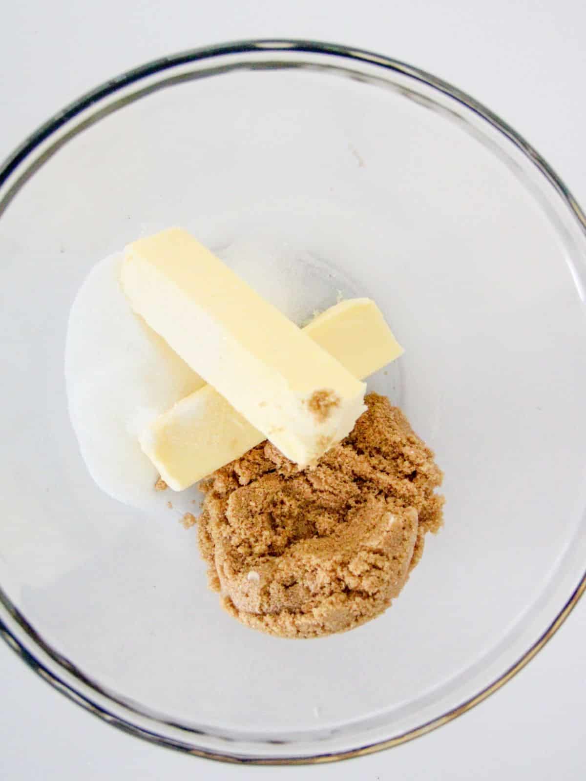 two sticks of butter, brown sugar and granulated sugar in clear bowl.