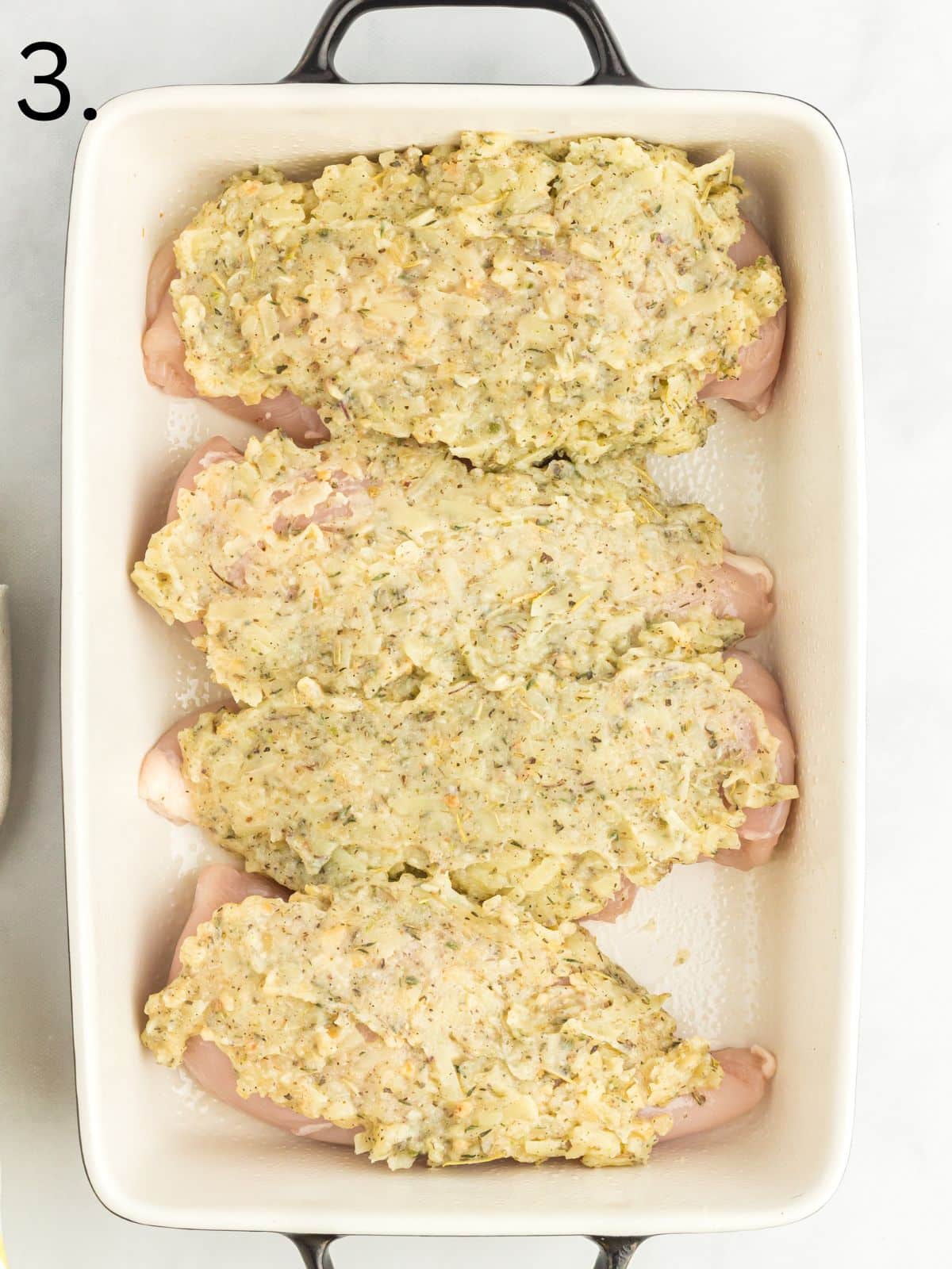raw chicken breasts in casserole dish with garlic butter and herbs on top.
