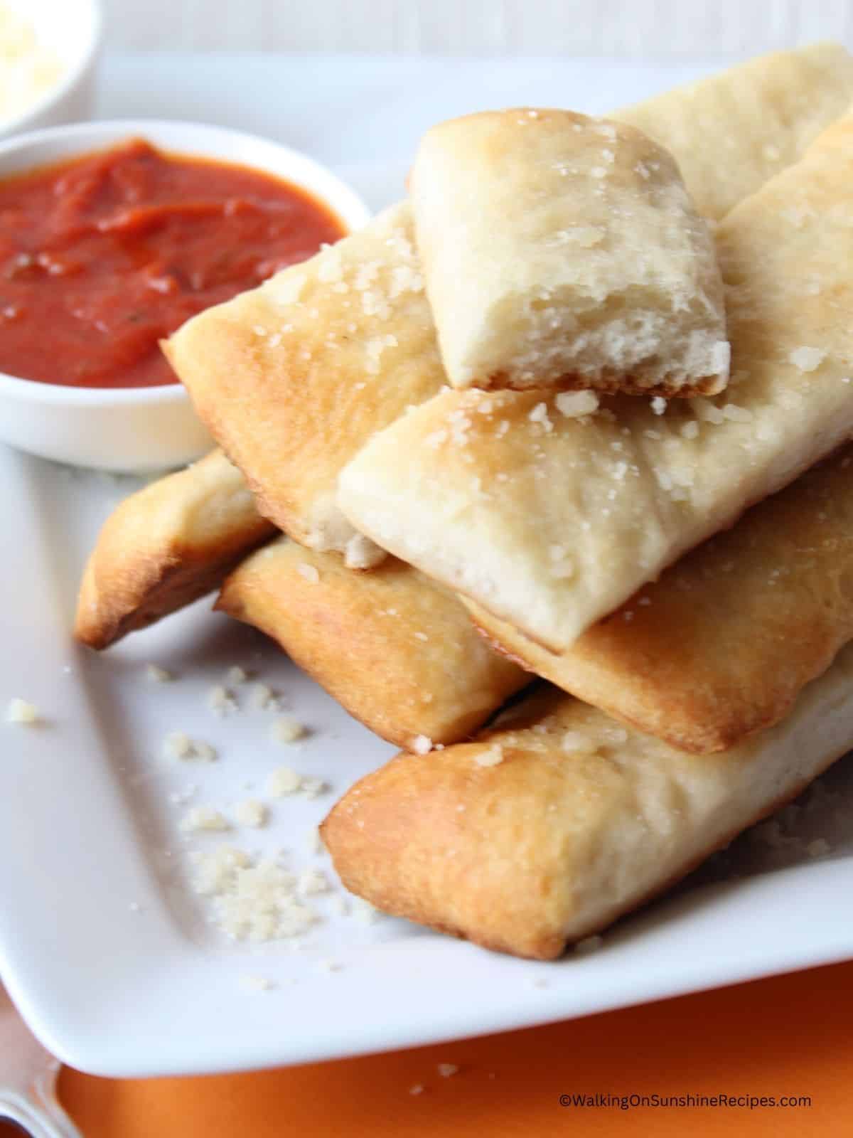 Breadsticks on white plate with small bowl of tomato sauce.