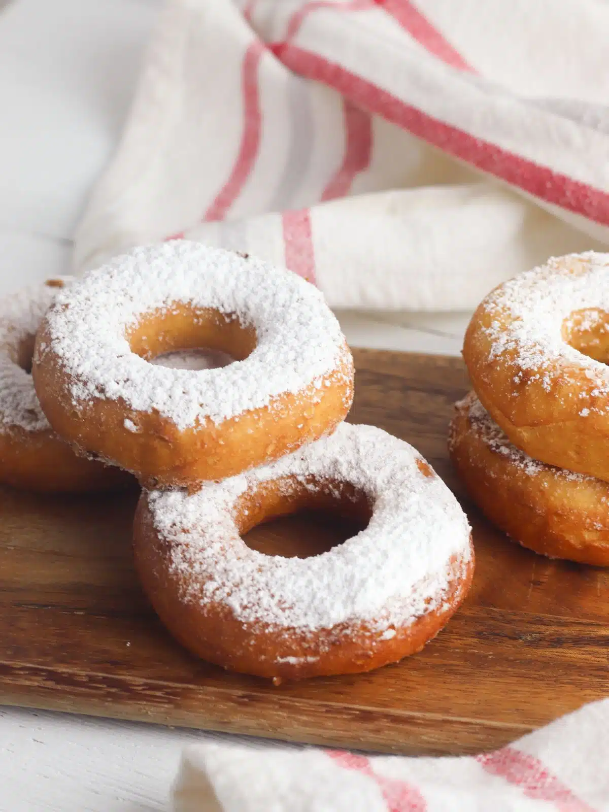 donuts with powdered sugar on cutting board and white with red stripe towel.