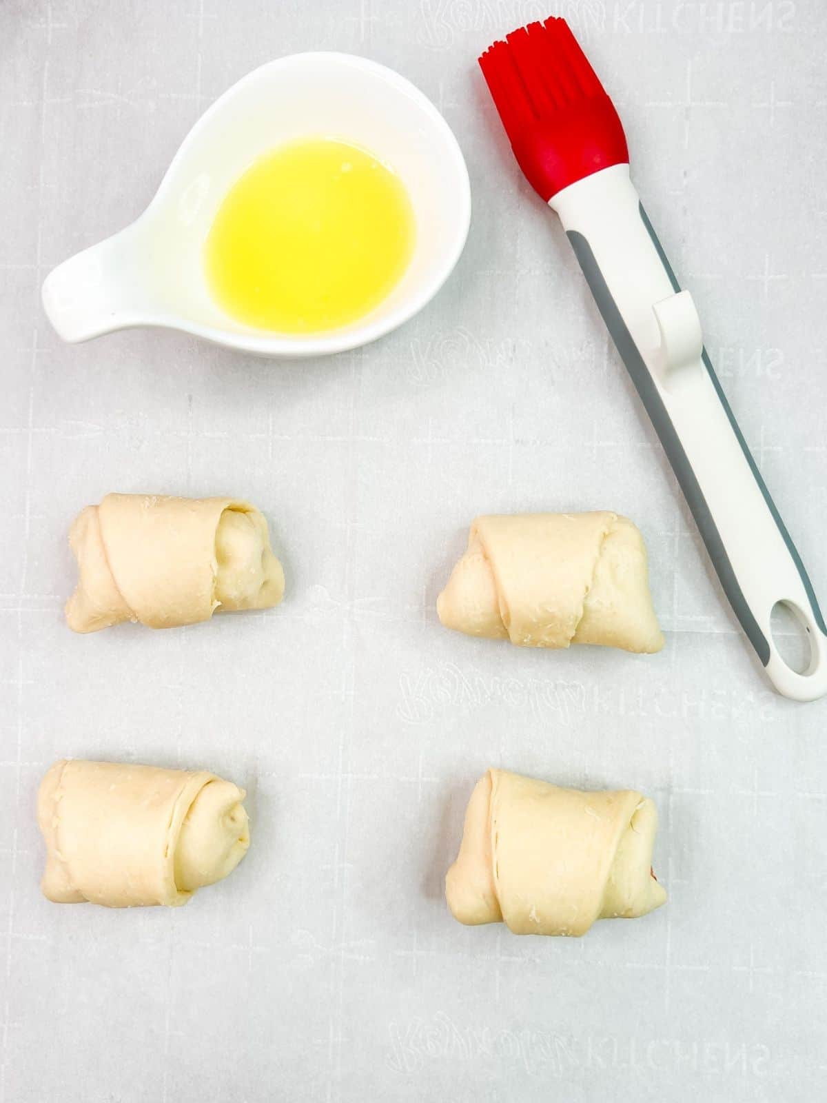 crescent roll bundles with melted butter in dish and silicone pastry brush.