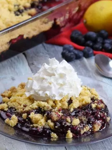 blueberry dump cake baked and served on plate with dollop of whipped cream on top.