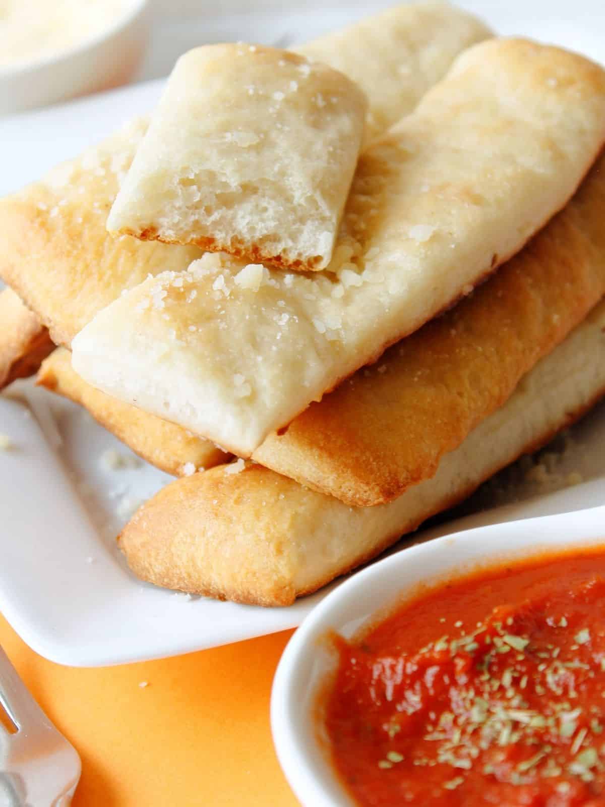 Baked breadsticks on white tray with bowl of marinara sauce.