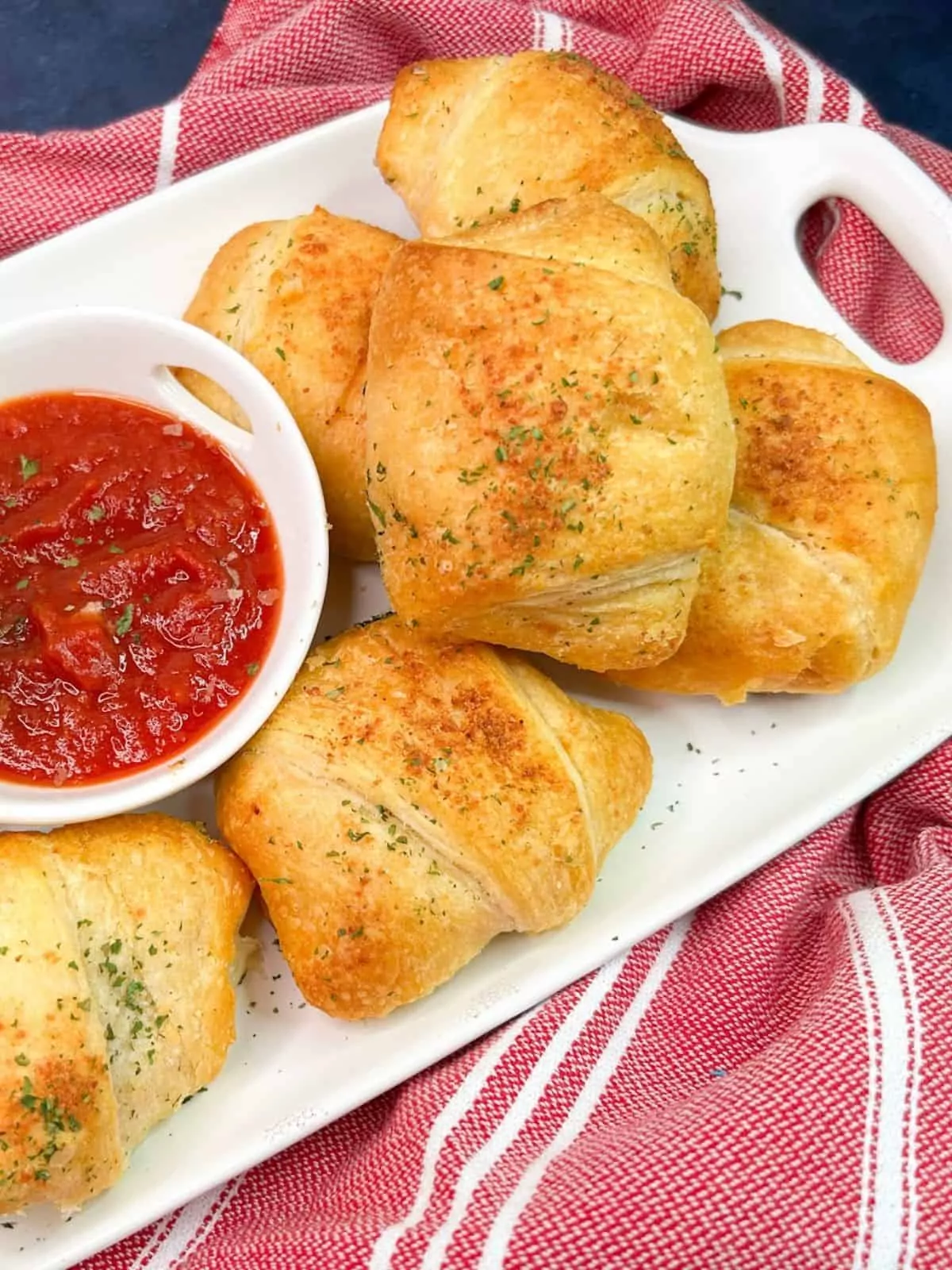 baked crescent rolls on white tray with small bowl of pizza sauce.