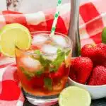 Sparkling water with strawberries, limes and simple syrup in glass with straw.