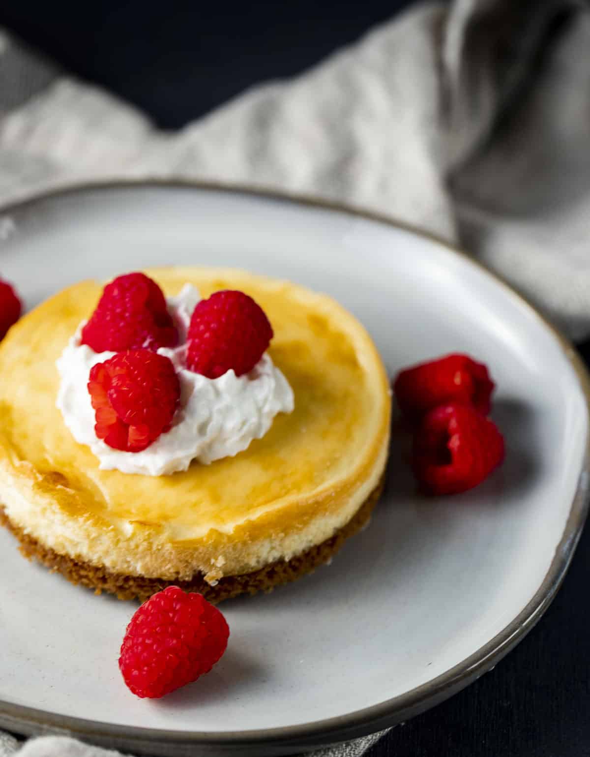small individual sized cheesecake with raspberries and whipped cream.