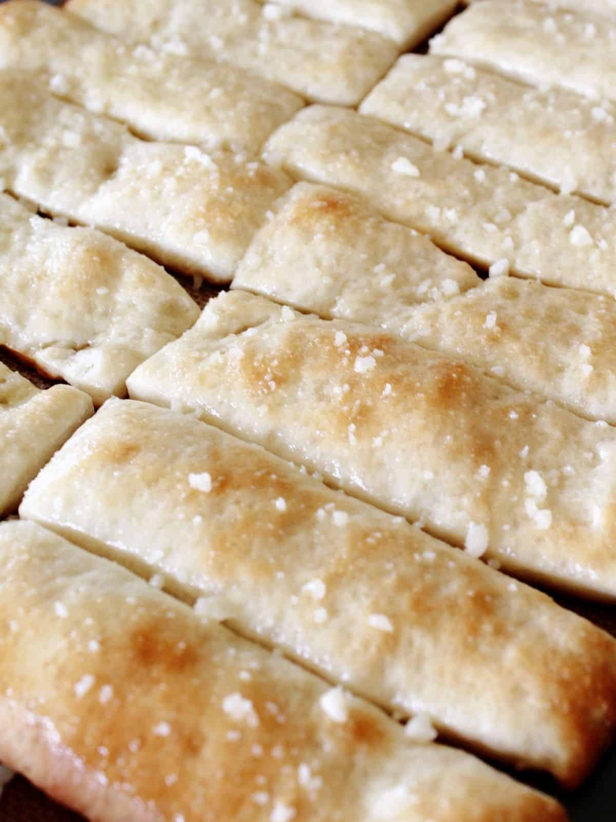 closeup of baked breadsticks on baking tray with Parmesan cheese sprinkled on top.