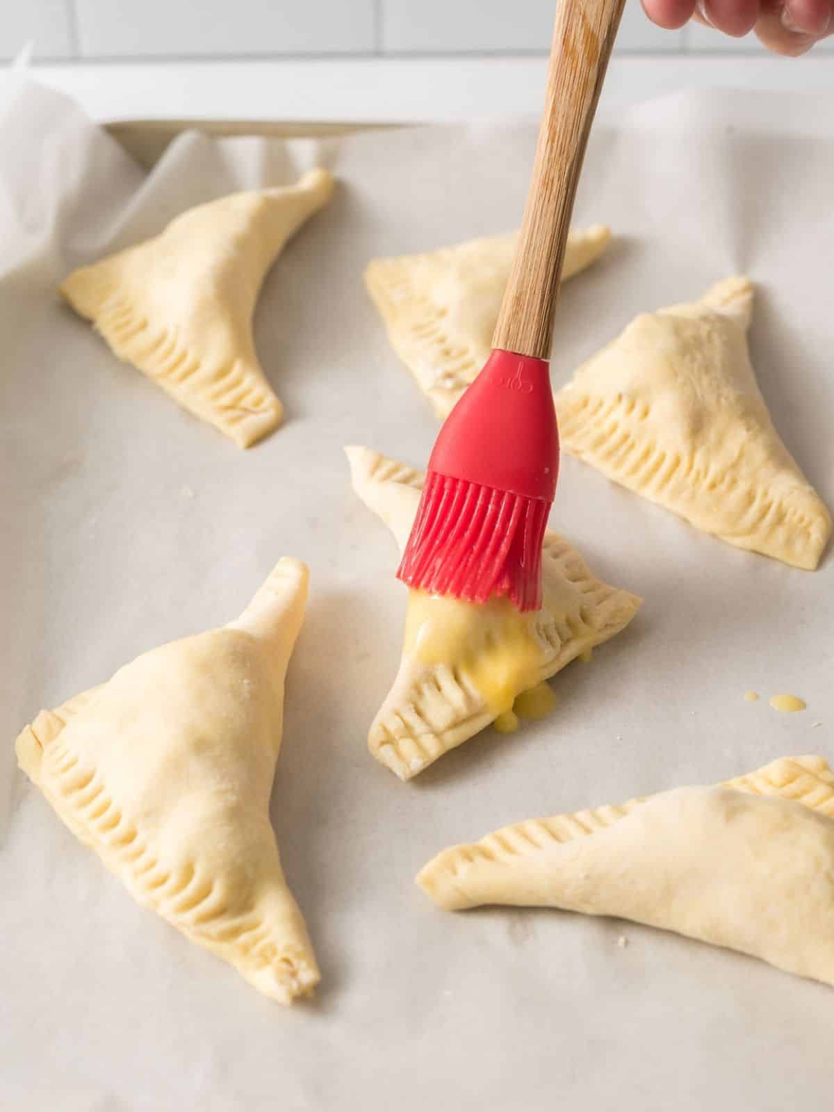 puff pastry pockets being brushed with egg wash with a red silicone pastry brush.