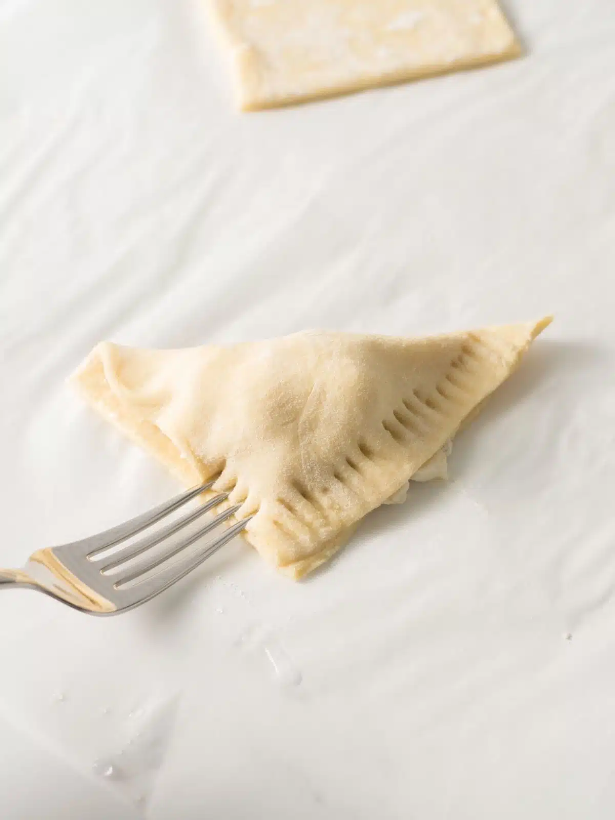 puff pastry folded into a triangle with a fork crimping the edges to seal in the filling.