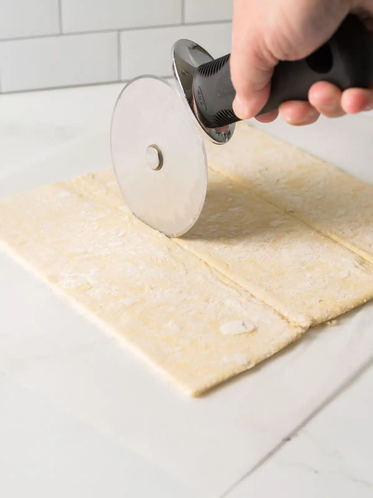 puff pastry being cut into thirds with a pizza cutter