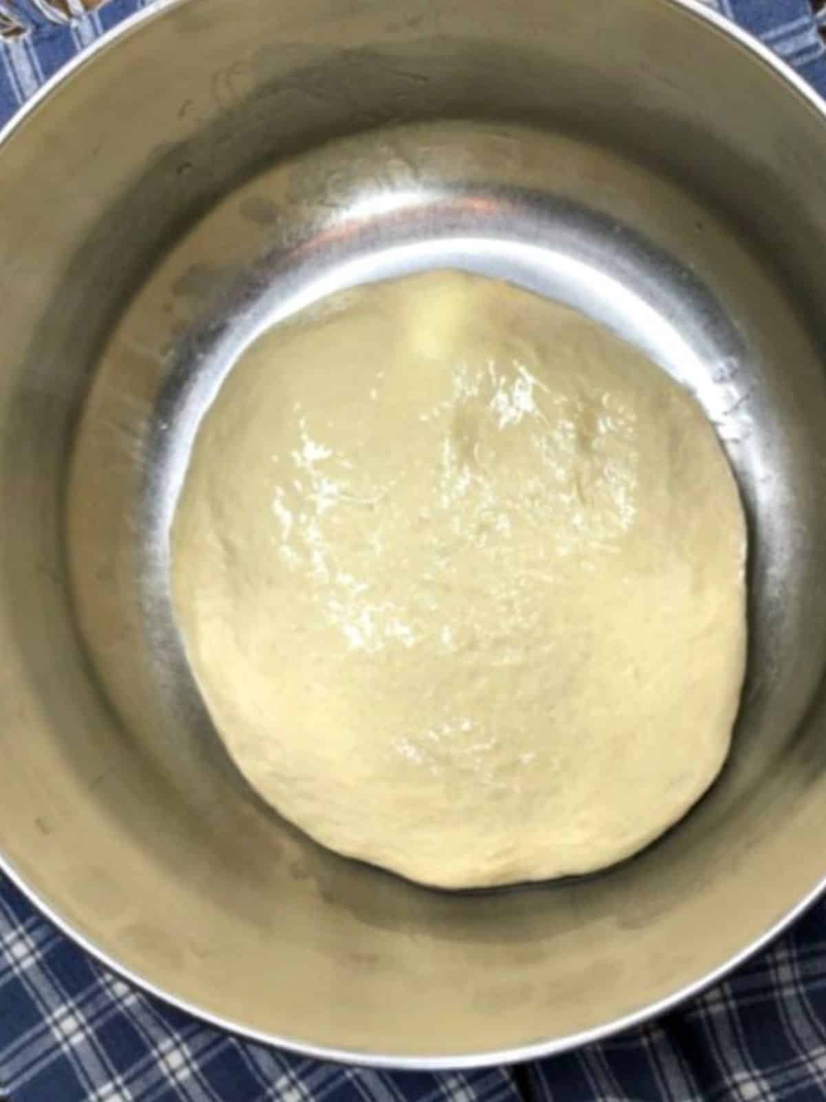 pizza dough before rising in metal bowl.
