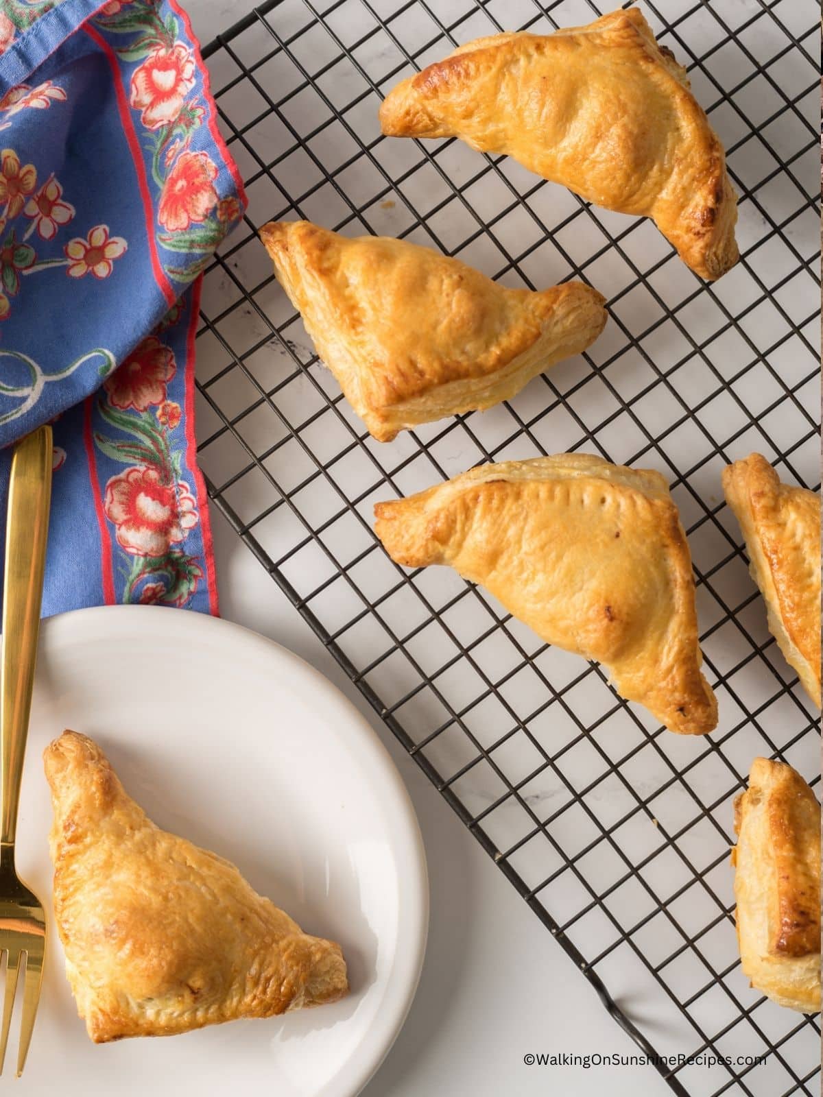 Chicken Puff Pastry Pockets on a cooling rack on the right. One is served on a white plate with a gold fork on the left.