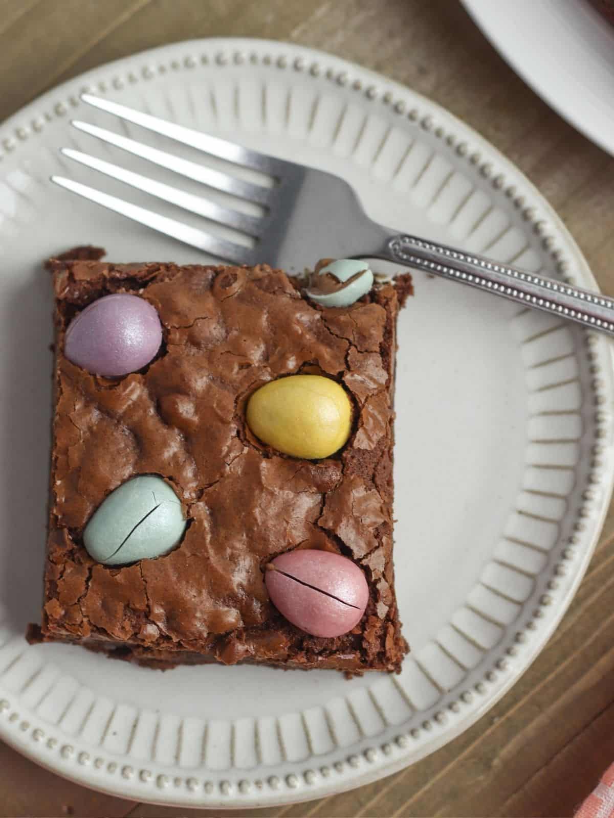 closeup of brownies with cadbury egg candy on white plate.