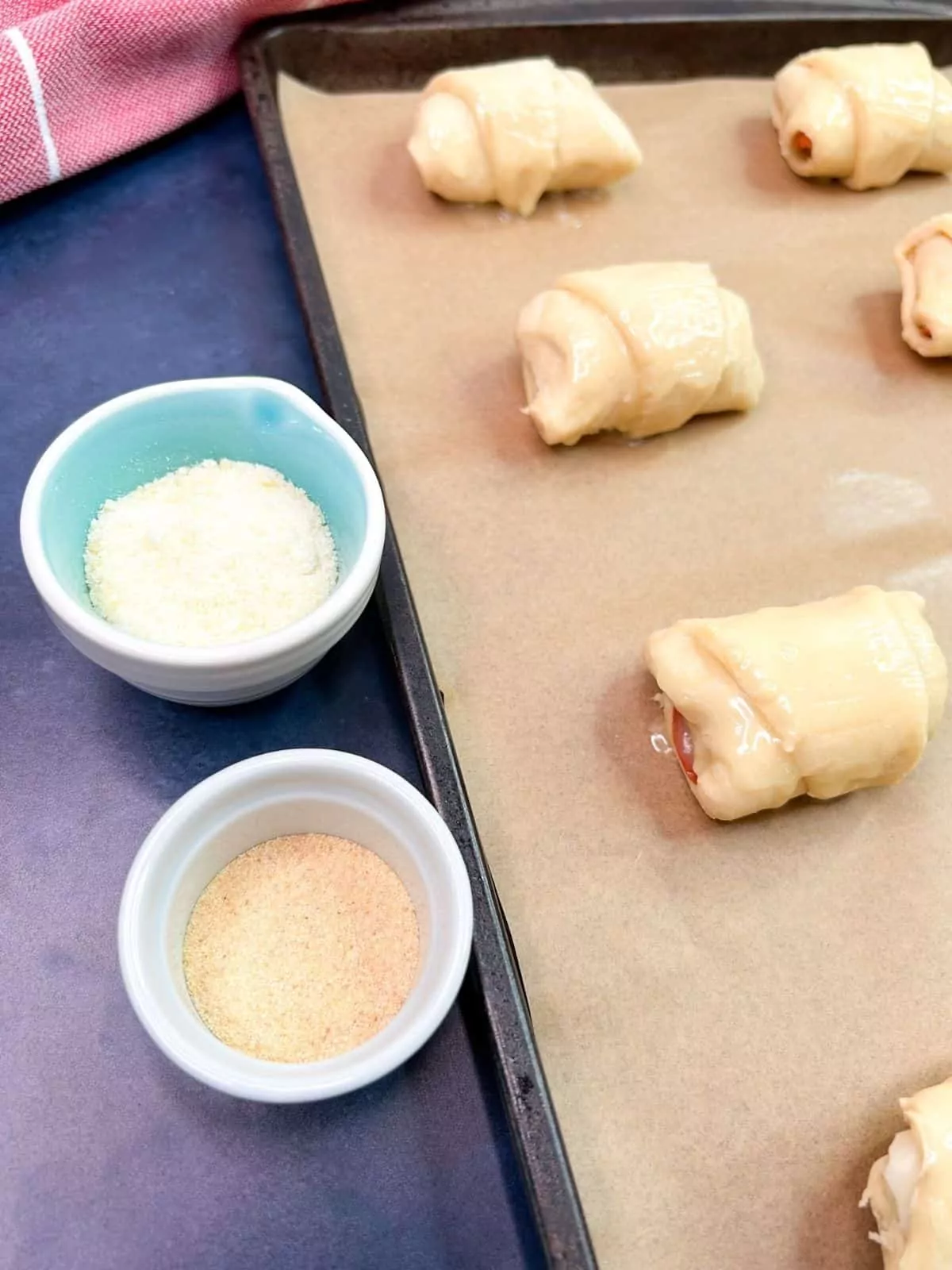raw crescent rolls on baking sheet with parchment paper. Two small bowls with Parmesan cheese and garlic powder.