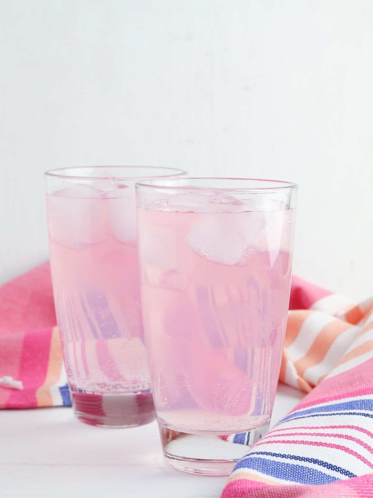 2 glasses of pink lemonade punch with striped towel.