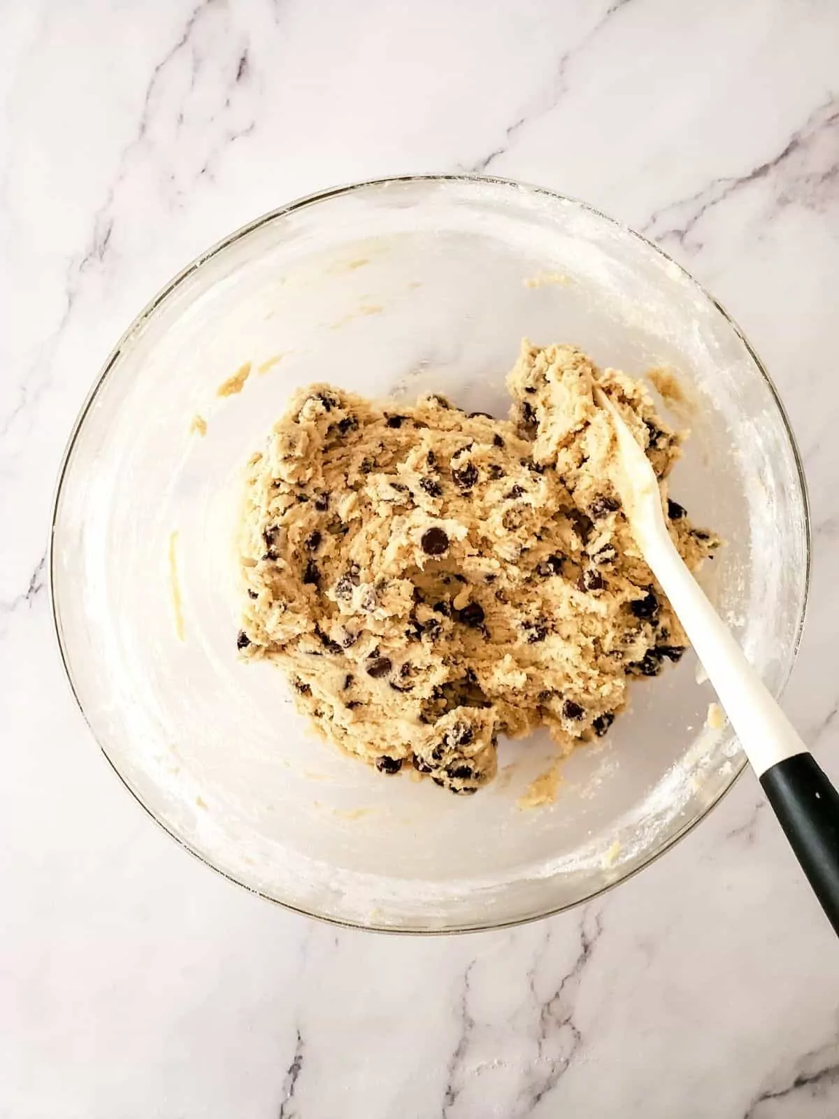 cookie batter with chocolate chips in bowl with rubber spatula.