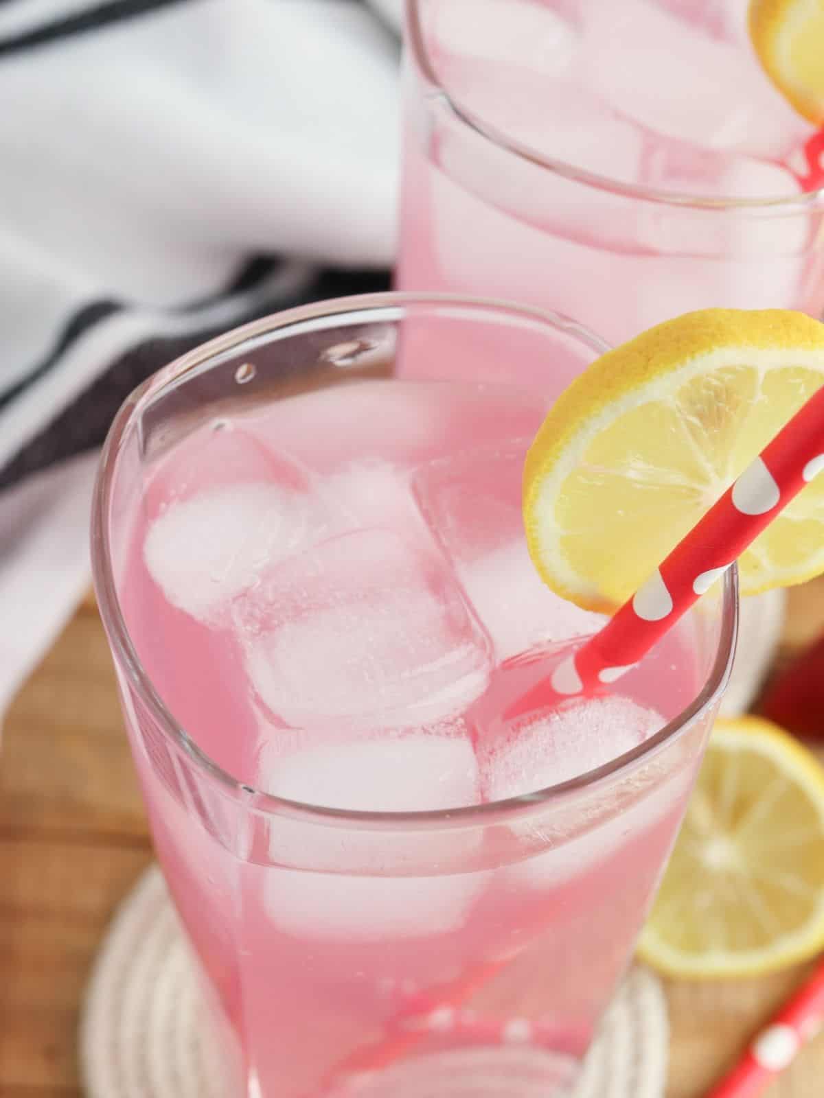 Overhead view of lemonade in glass with ice cubes, lemon slices and straw.