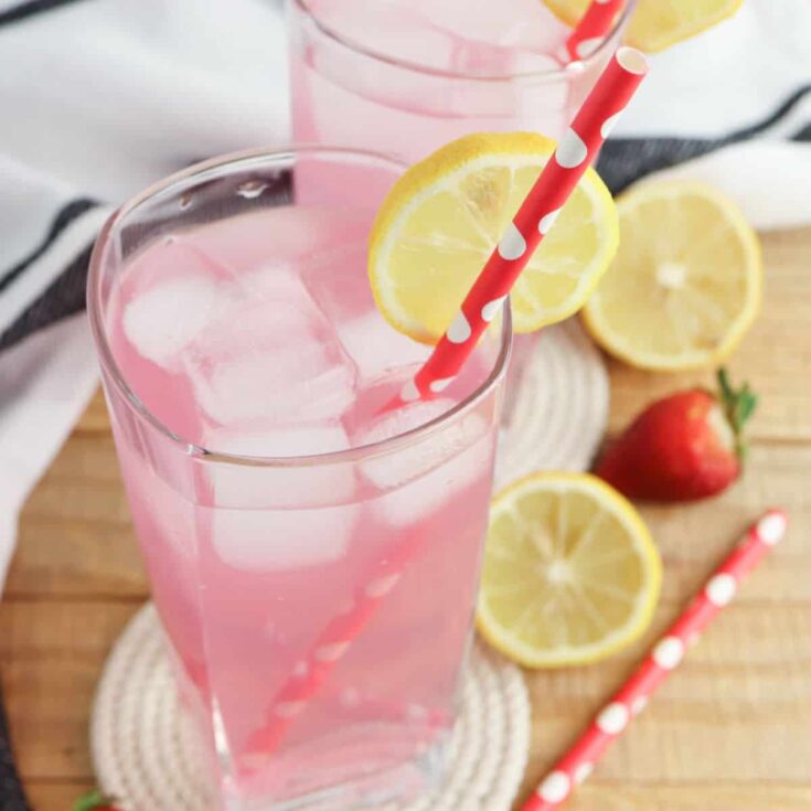 strawberry lemonade in glass with lemon slice in cup and on table top with straw.