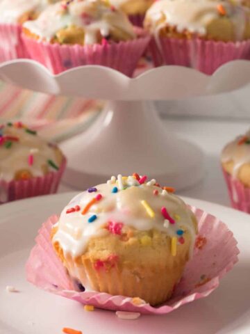 Muffins with sprinkles and glaze on plates.