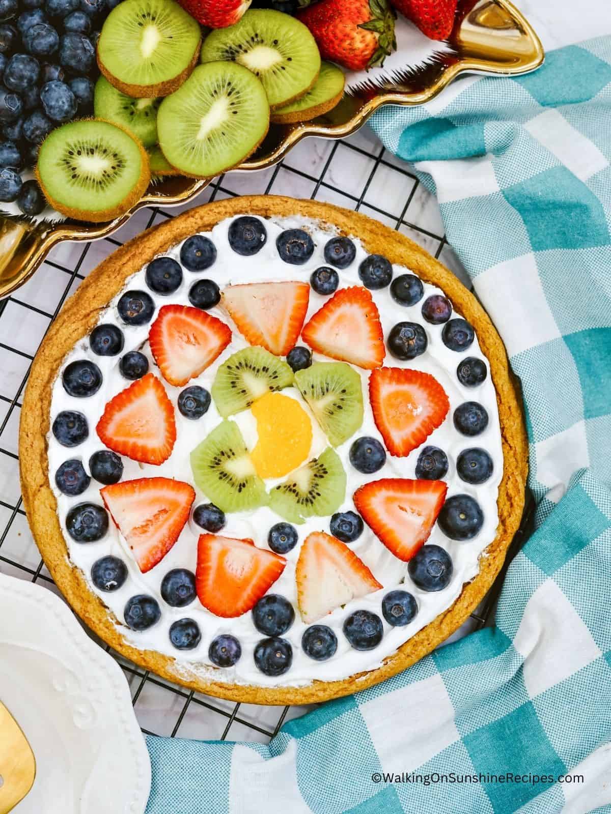 Overhead view of dessert pizza made with sugar cookie dough, mixed fruit and whipped topping.