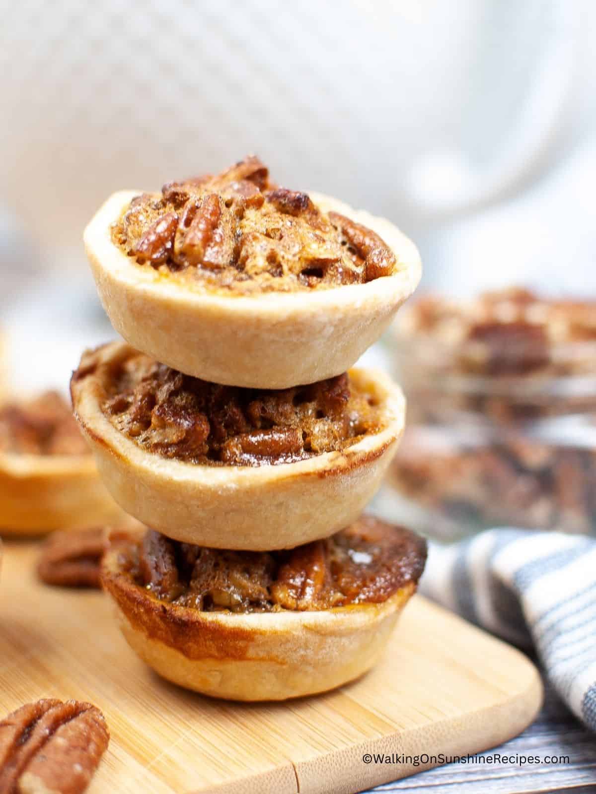 Pecan pie tartlets stacked on top of each other on cutting board.