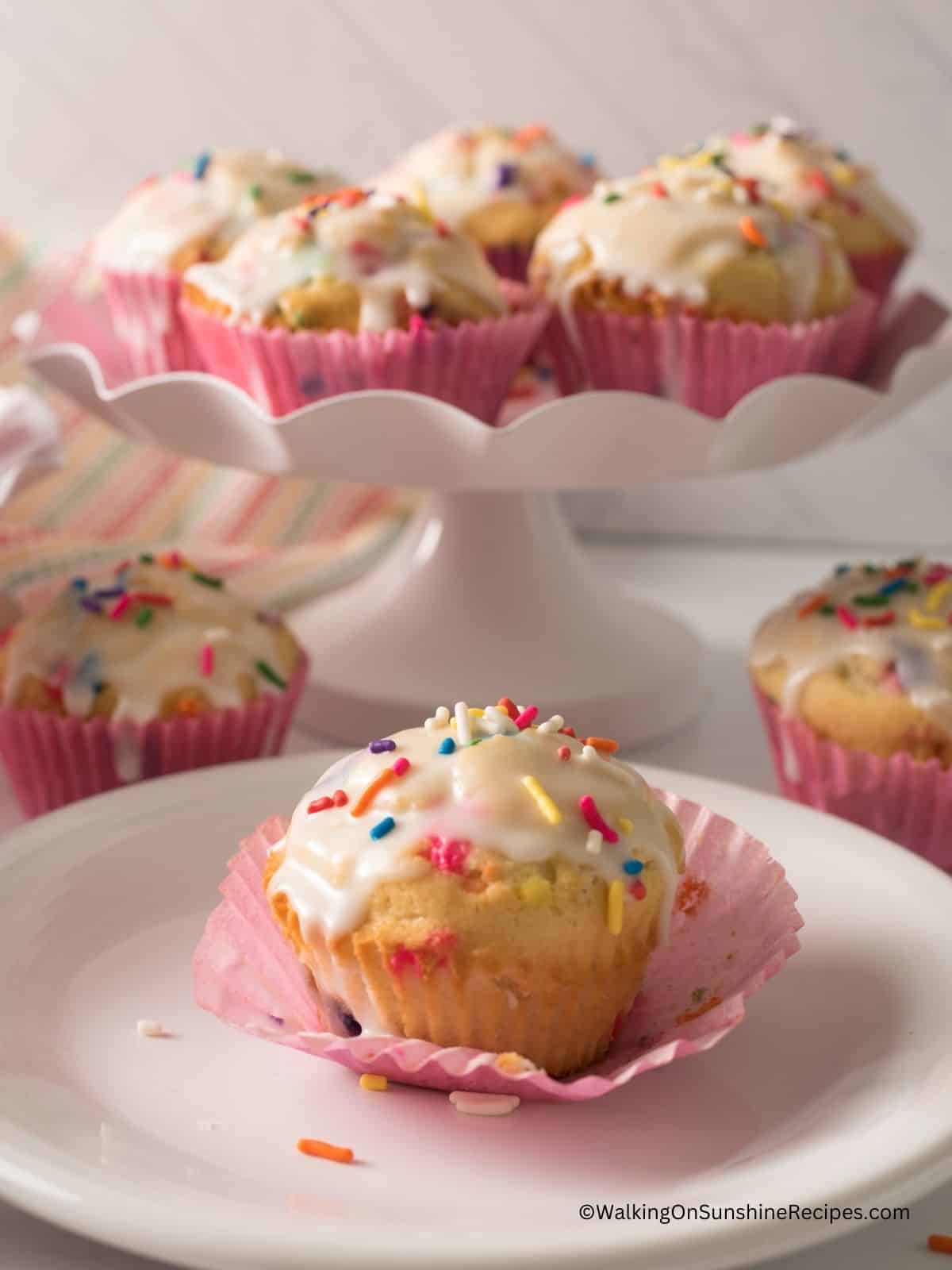 birthday muffins with sprinkles and powdered sugar glaze on plate and cake stand.